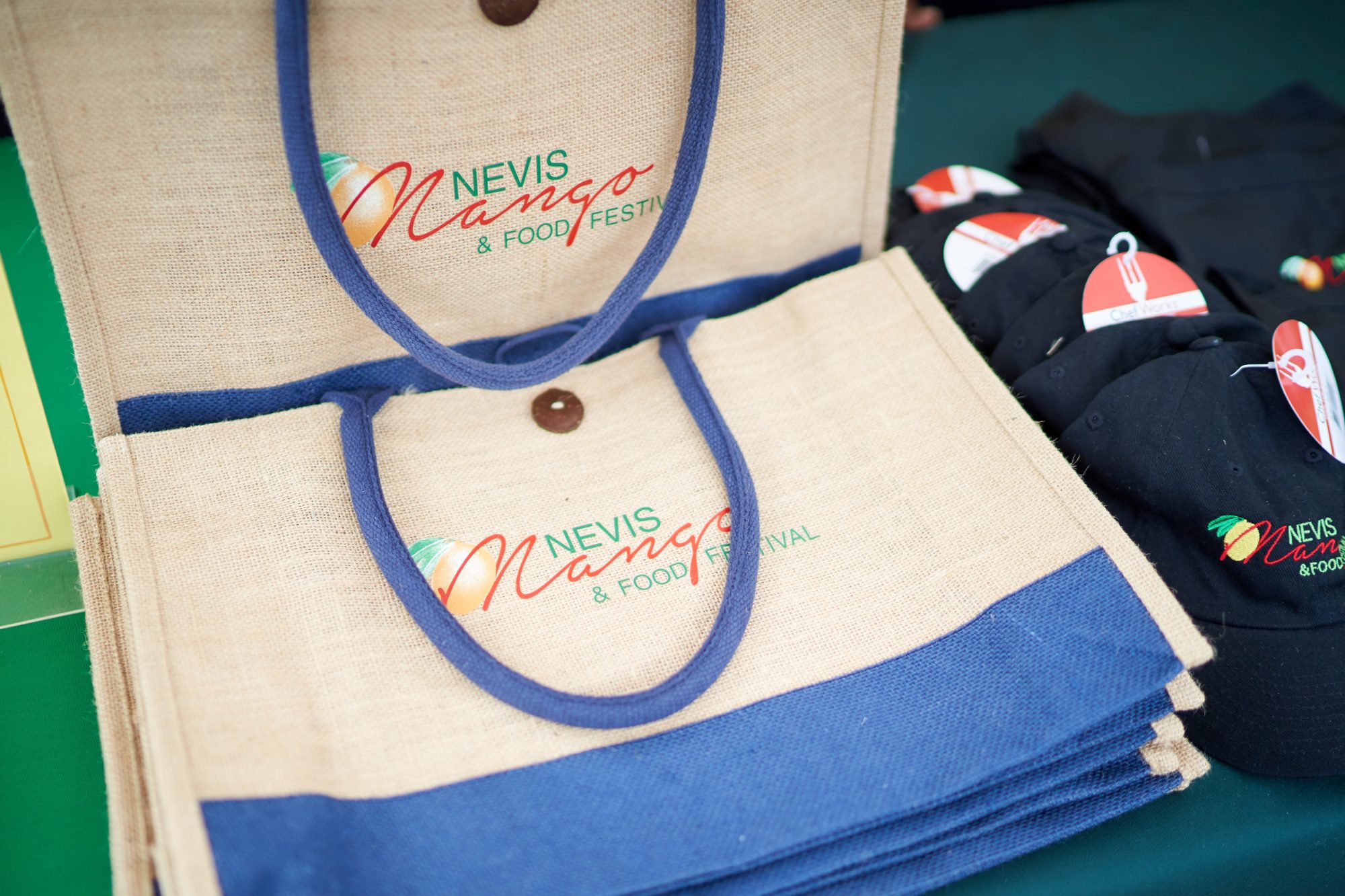 Nevis Mango & Food Festival branded tote bags and caps on a vendor table