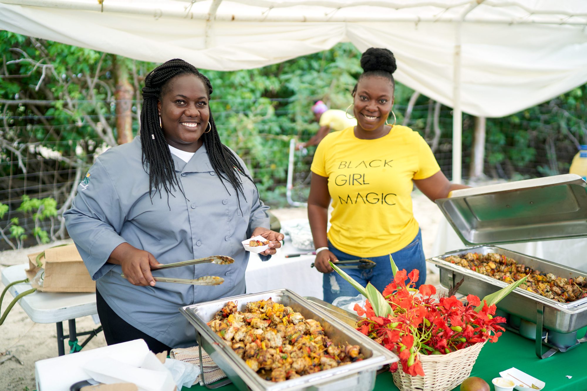 Two smiling women serving local food at a Nevis Mango Festival tasting stall