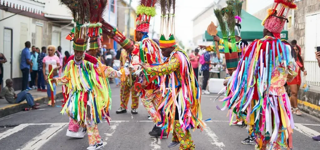 Masquerade troupe in ribboned costumes and peacock-feather headdresses dancing in the street during Nevis Culturama