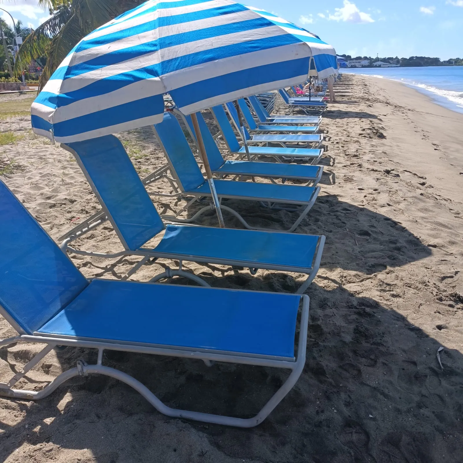 Blue loungers under striped umbrellas on the sand at Ganzies, Pinney's Beach, Nevis