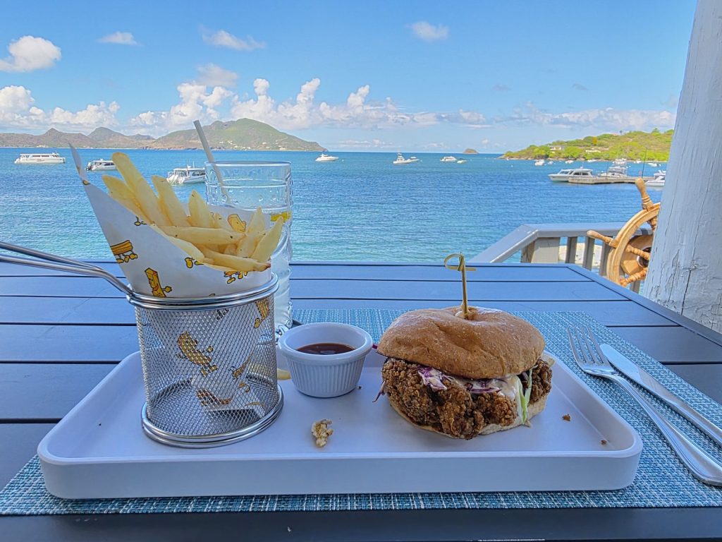 A sandwich and a basket of fries on a table at On The Rocks on Nevis, with boats on the water and St Kitts in the background