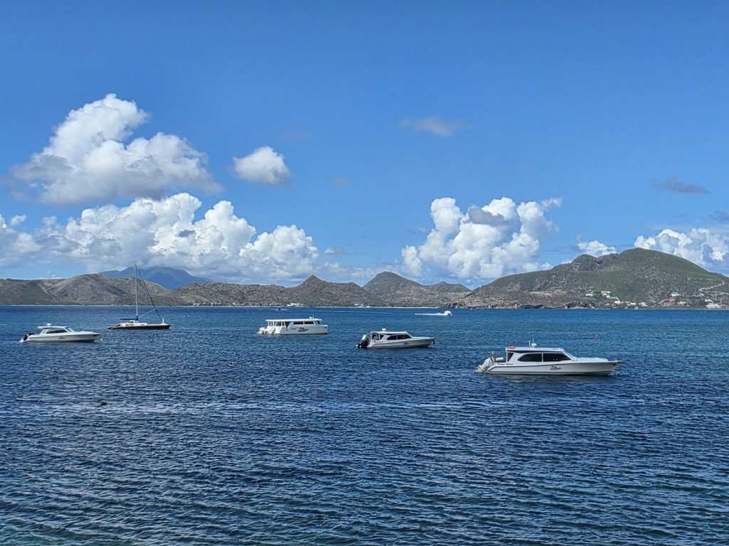 Boats on blue water, seen from On The Rocks on Nevis, with the hills of St Kitts across the channel under a clear sky